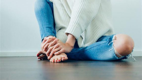 Photo of woman sitting on floor, clutching her ankle